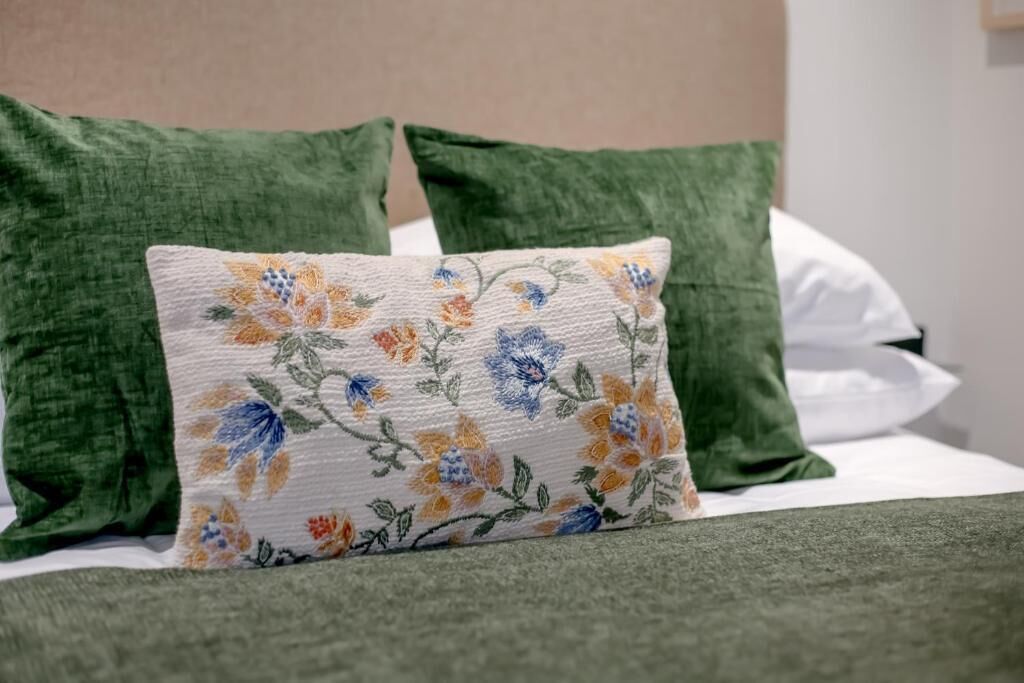 Un lit avec des oreillers verts et un coussin à motifs floraux.