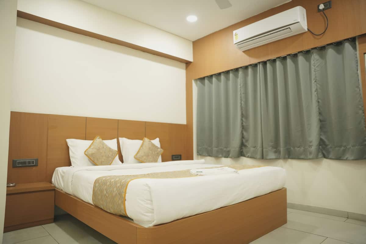 A hotel room with a wooden headboard, a bed with white bedding, a nightstand, and an air conditioning unit mounted on the wall.