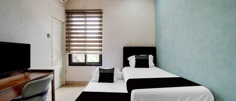 A bedroom with two beds, a desk with a chair, a TV, and an air conditioning unit.