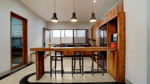 A kitchen with a wooden island, bar stools, pendant lights, and a view through the window. - OYO 95214 Ohana Residence Karawaci (Curug)