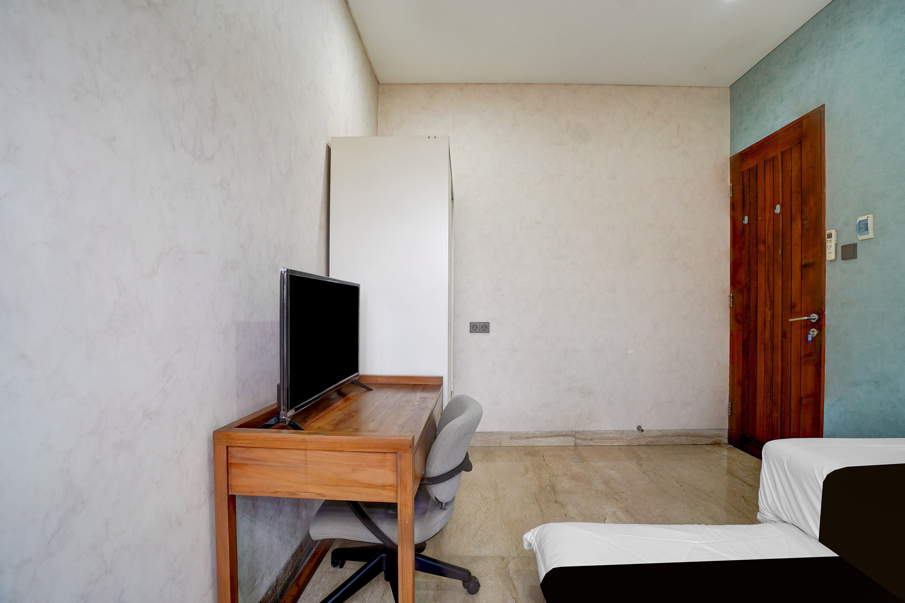 A room with a wooden desk, a television, a bed, and a door.