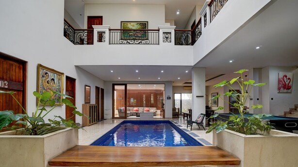 A spacious indoor area with a central pool, wooden benches, and a staircase leading to an upper level. - OYO 95214 Ohana Residence Karawaci (Curug)