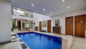 A swimming pool with a tiled deck, wooden doors, and a balcony. - OYO 95214 Ohana Residence Karawaci (Curug)