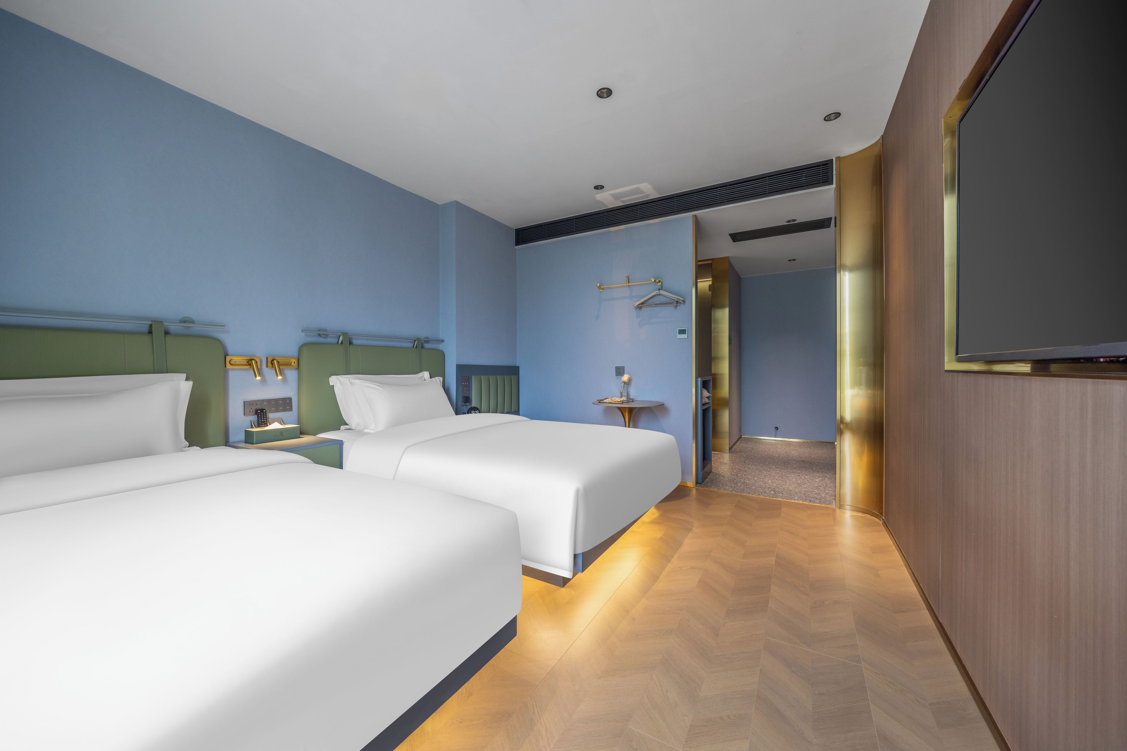 Habitación de hotel con dos camas, un televisor, una mesita de noche y una pequeña mesa con un florero.