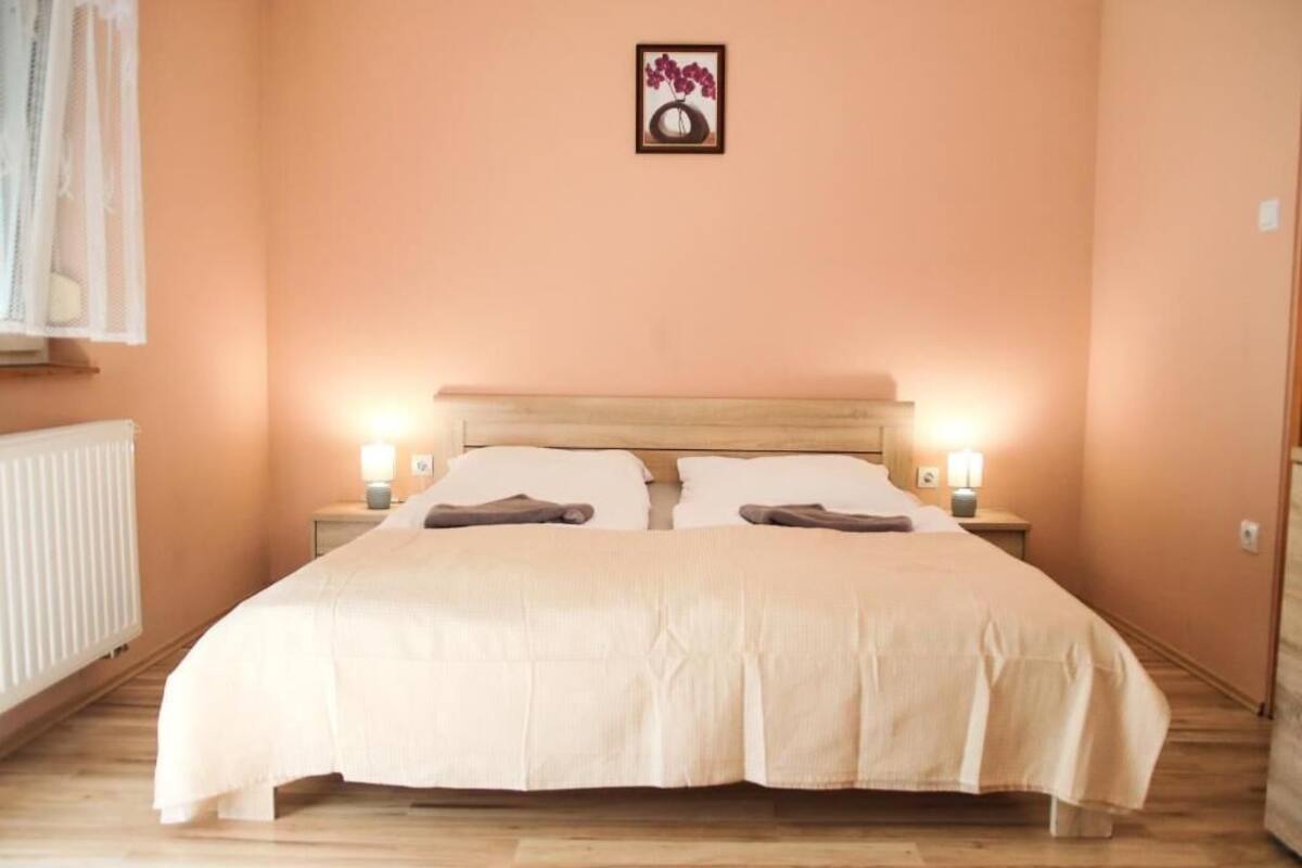 A bedroom with a bed, two bedside lamps, a framed picture on the wall, and a window with a curtain.