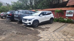 Ein Parkplatz mit mehreren SUVs, ein rot backengebautes Gebäude mit der Aufschrift "taman resort" und ein gepflasterter Weg.