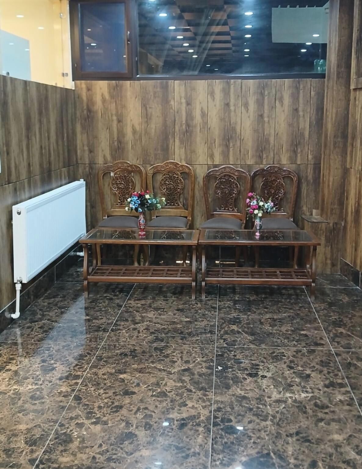 A room with a wooden wall, a radiator, a marble floor, and a table with chairs.