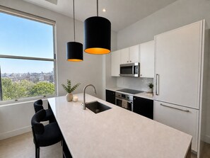 A modern kitchen with a large island, white cabinetry, stainless steel appliances, and pendant lighting. - Central Park - Luxury 4BR Apartment - Morningside Drive (New York)