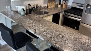 Eine moderne Küche mit weißen Schränken, einer Granit-Arbeitsplatte, einem Edelstahl-Kühlschrank und einem eingebauten Backofen.