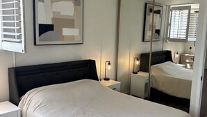 Ein Schlafzimmer mit einem Bett, Nachttischen, einem Deckenventilator, einem großen Spiegel und einem Fenster mit Jalousien.
