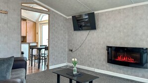 Een woonkamer met een open haard, een aan de muur bevestigde televisie en een zichtbare eetruimte door een open deur.
