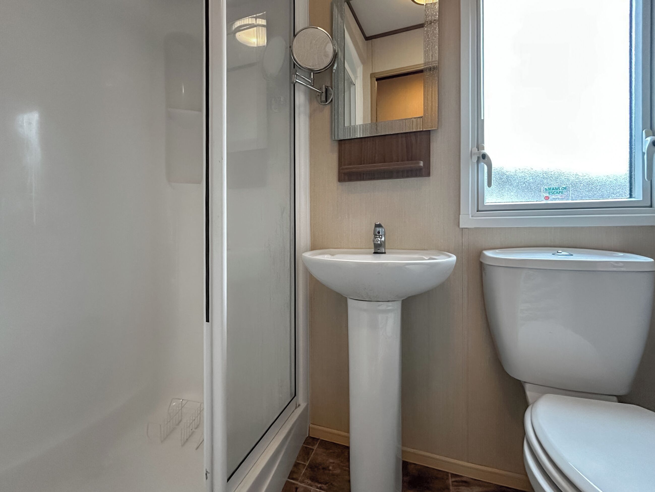 A bathroom with a shower, sink, toilet, and a window.