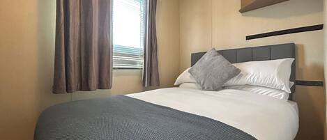 A hotel room with a bed, a window with curtains, a headboard, and a shelf above the bed.