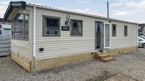 A mobile home with a sign reading 'Havern,' a window with curtains, and a small porch area.