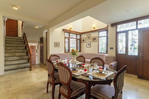 A dining area with a round table, striped upholstered chairs, and a staircase leading to another room. - Jobner Haus - A Boutique Homestay (Jaipur)