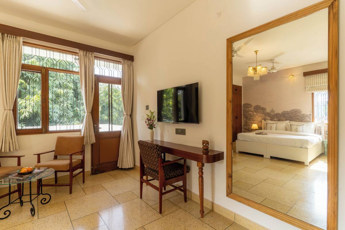 Una habitació amb llit, televisió, taula, cadires i un gran mirall que reflecteix una altra habitació.