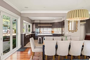 A modern kitchen with dark cabinetry, a central island, and a dining area with six chairs.