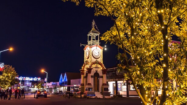 A clock tower with a clock face, surrounded by illuminated trees and buildings.