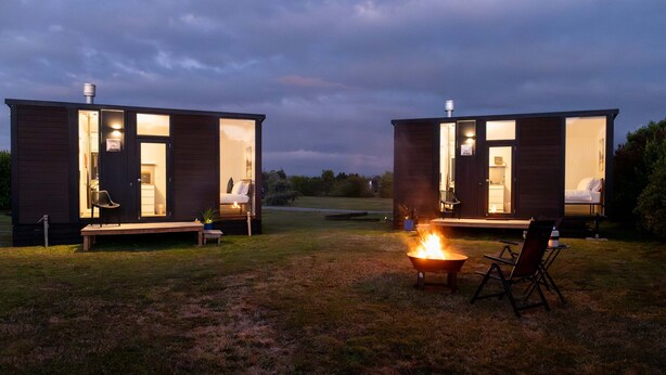 Two cabins with open doors, a fire pit, and a bench.