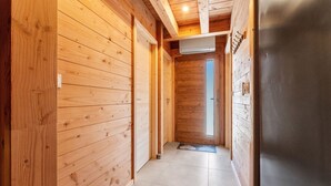 Un pasillo interior de madera con suelo de baldosas, una puerta al final y un refrigerador a la derecha.
