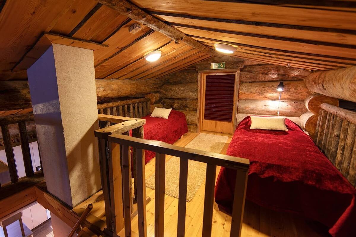 Una cabaña con interior de madera, un balcón y una cama con una manta roja.