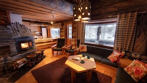 A cozy cabin interior with a fireplace, wooden furniture, and a view of the snowy outdoors. - Rukan Salonki Resort (Kuusamo)