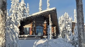 A log cabin with a large window, wooden walls, and a snow-covered roof. - Rukan Salonki Resort (Kuusamo)