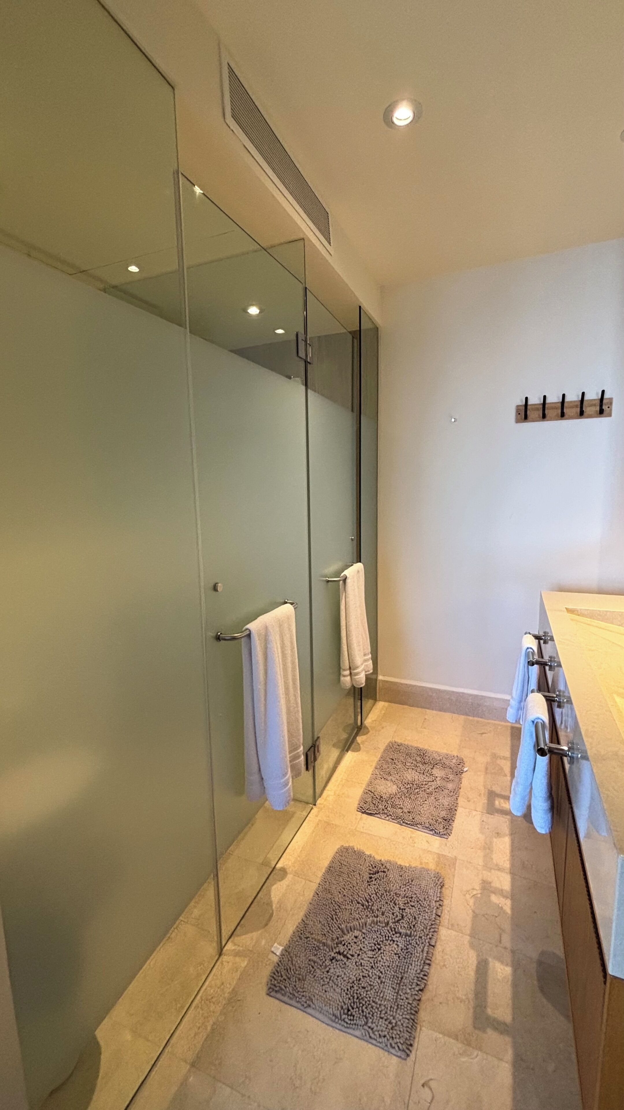 A modern bathroom with a glass shower enclosure, a sink with a towel rack, and two textured rugs on the floor.
