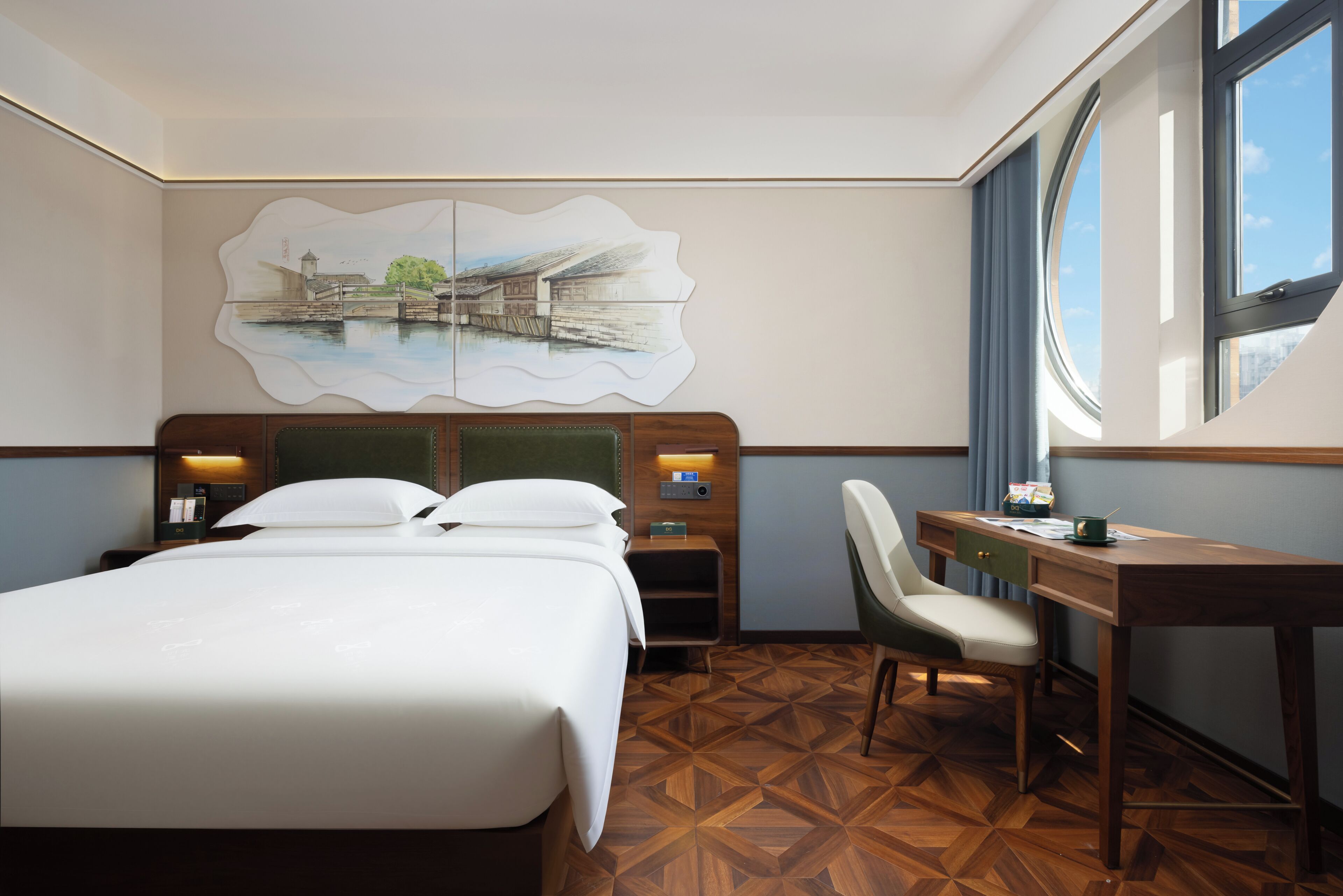 A hotel room with a bed, desk, chair, and a painting on the wall.