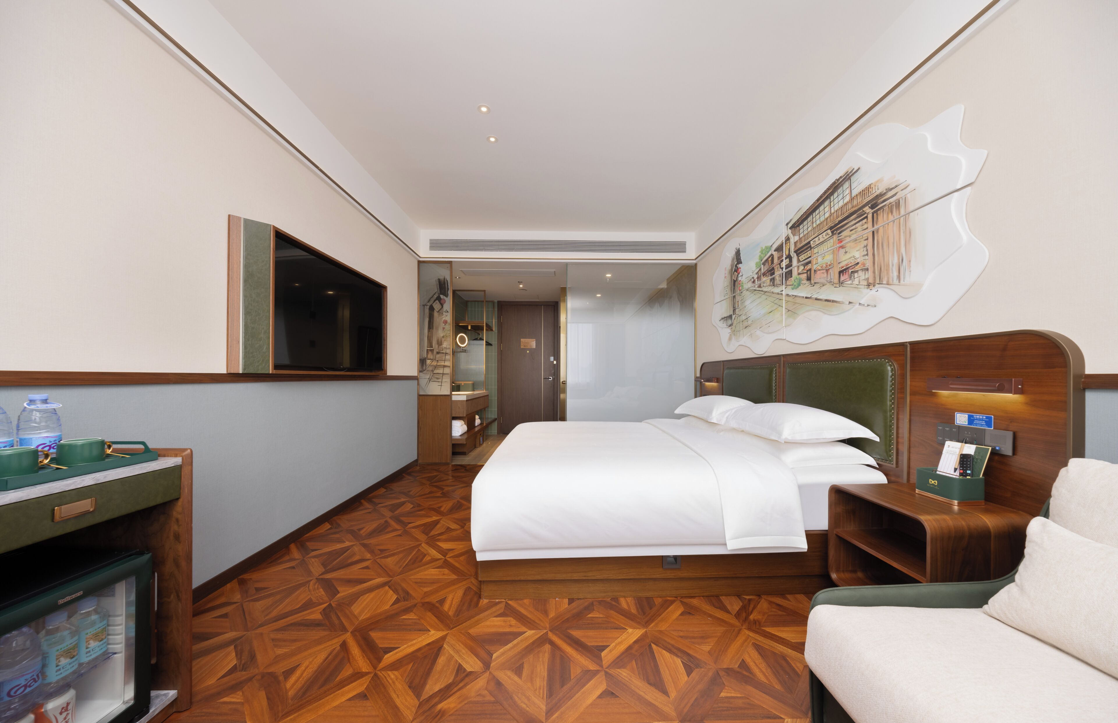 Une chambre d’hôtel avec un lit, un bureau doté d’un réfrigérateur, une chaise, un tableau au mur et un plancher en bois.