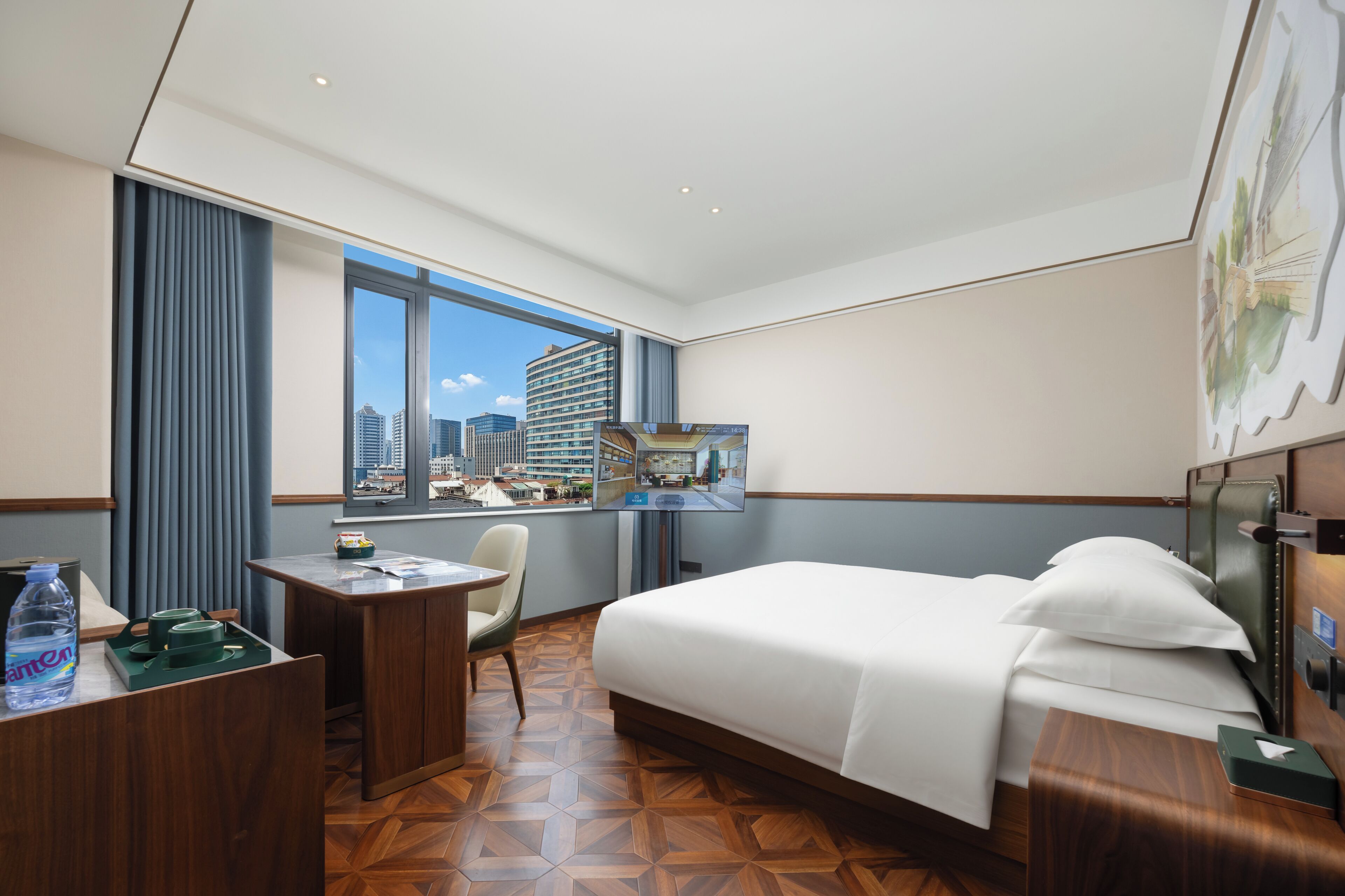 Habitación de hotel con cama, escritorio, silla y una ventana grande que ofrece vistas a la ciudad.