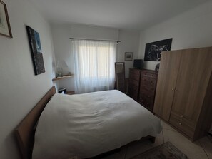 A bedroom with a bed, a dresser, a mirror, and a window with curtains. - Charming 1-Bedroom Apartment in Alpes-Maritimes (Alpes-Maritimes)