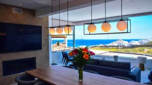 Un comedor moderno con una mesa de madera, sillas, un jarrón de flores y una pantalla de televisión grande.
