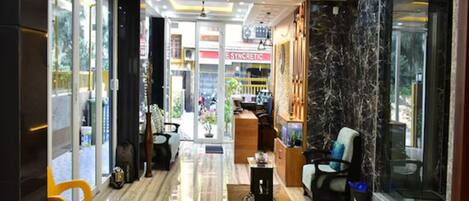 A hotel lobby with a marble floor, a reception desk, seating area, and a view of the street.
