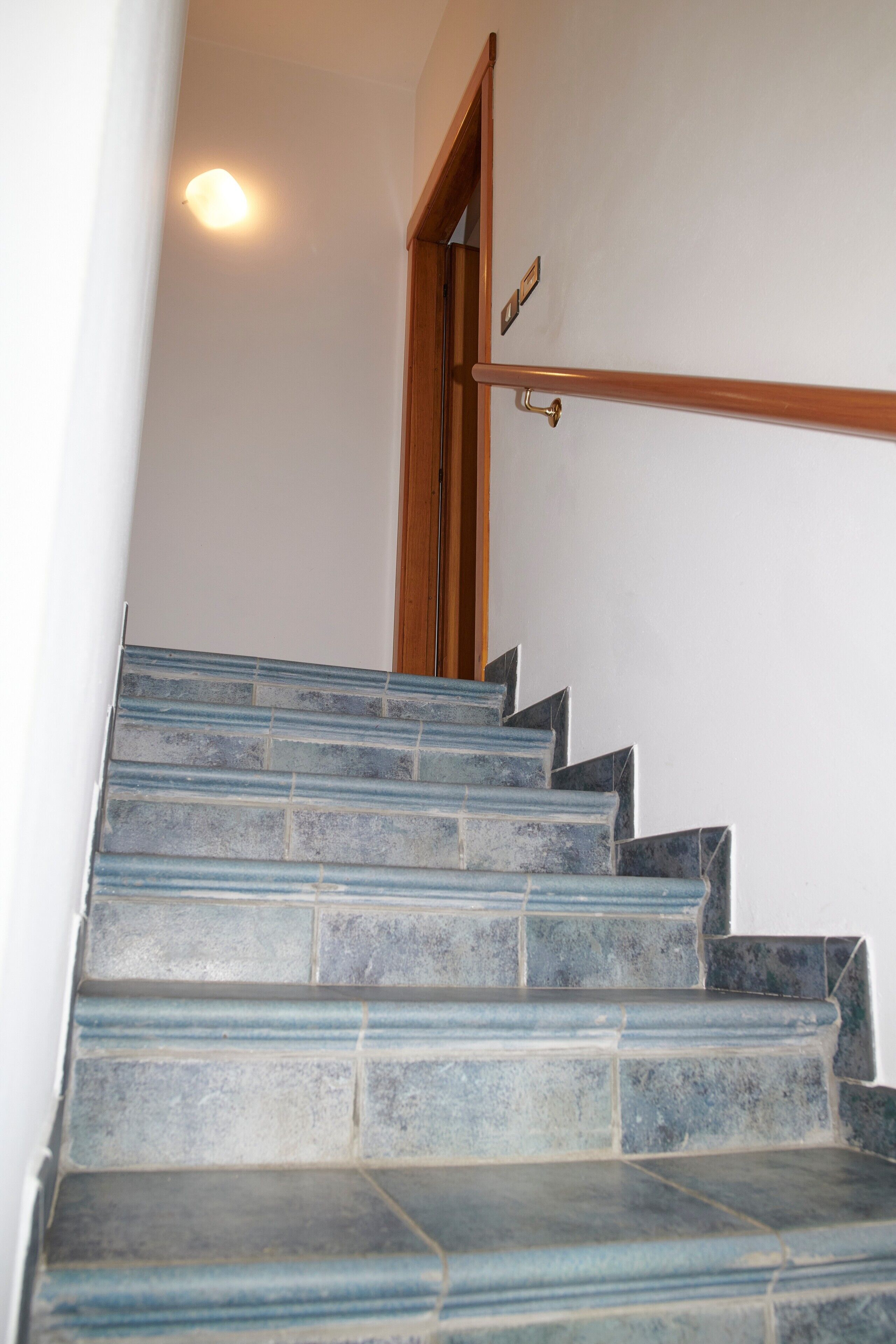 Uma escadaria com azulejos azuis, um corrimão de madeira e uma porta com puxador de latão.