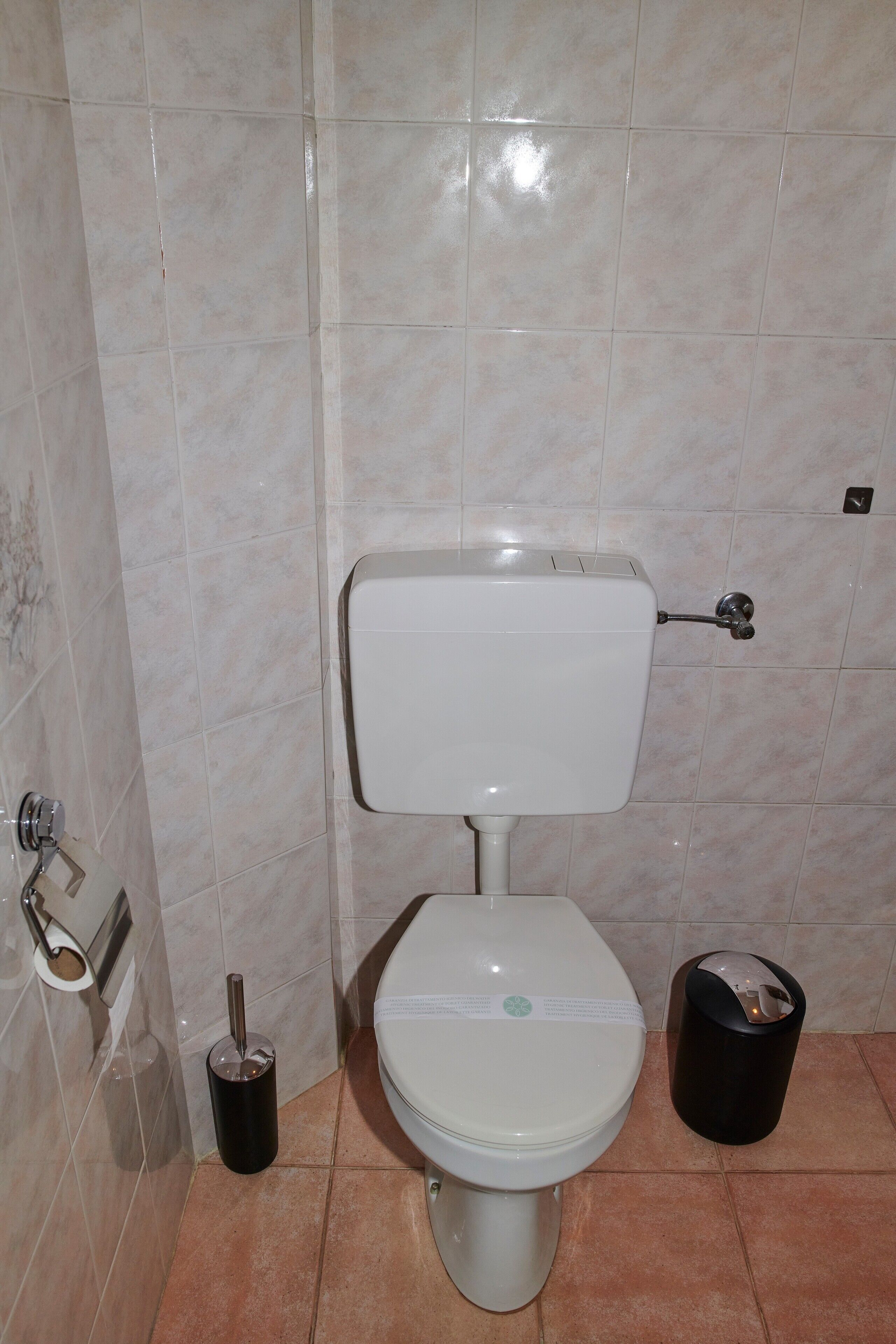 Un bagno con un water, un cestino e una spazzola per il water.