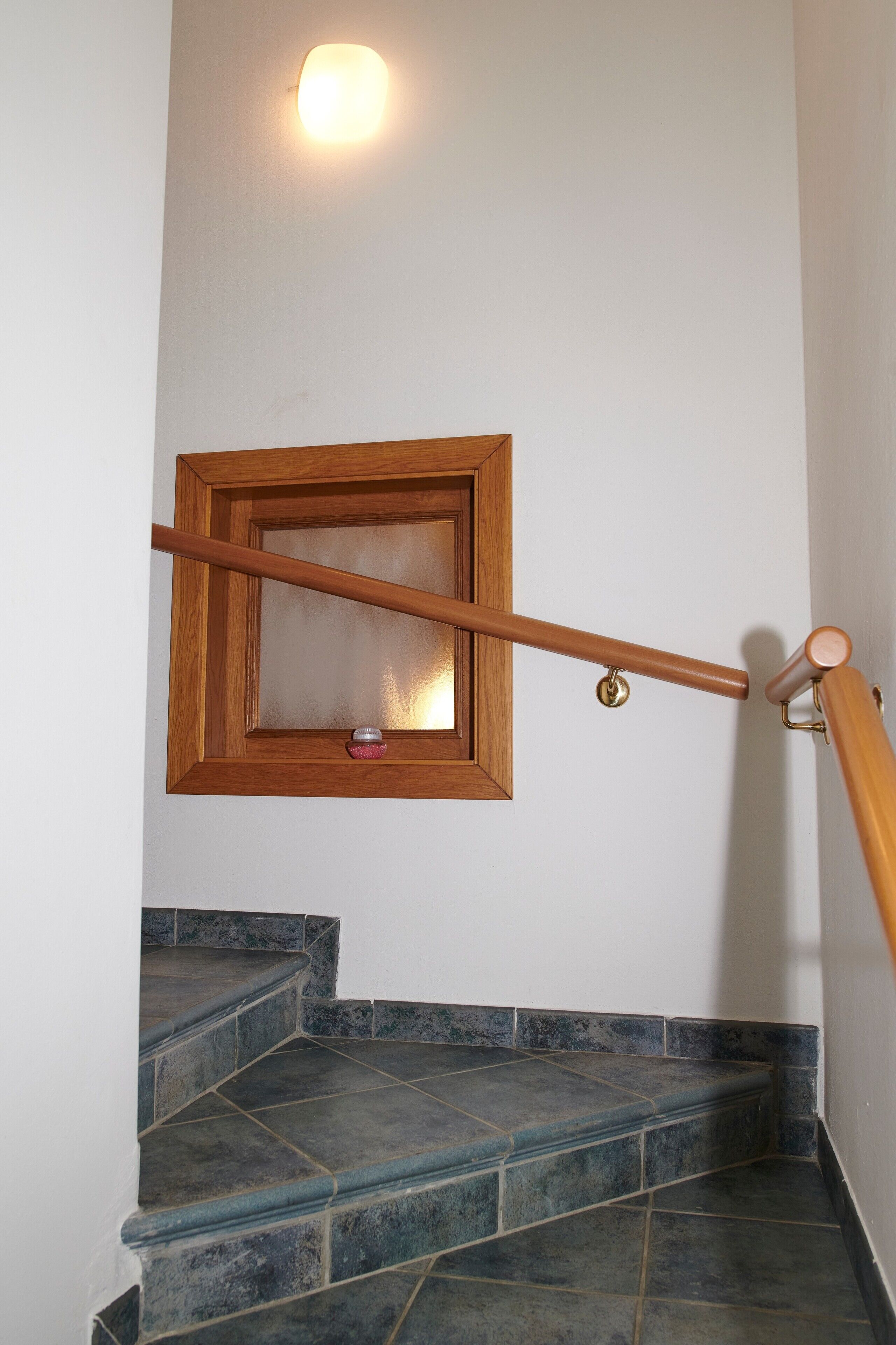 A staircase with a wooden handrail, a glass door, and a wall-mounted light fixture.