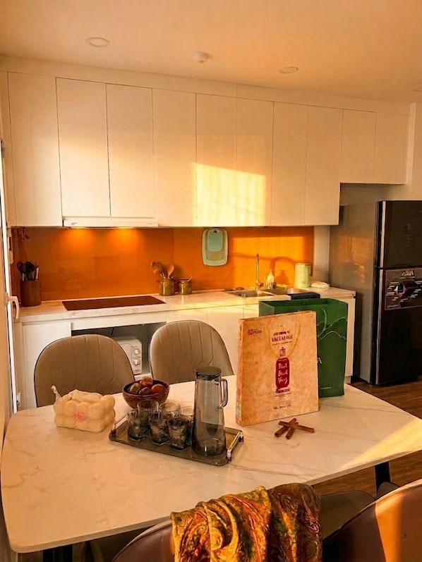 Uma cozinha moderna com armários brancos, uma geladeira de aço inoxidável e uma mesa de jantar posta com um jarro, copos e um saco de petiscos.