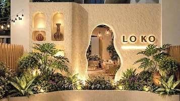 A modern building with a sign reading 'LO KO' and a well-lit entrance with plants and seating areas visible inside.