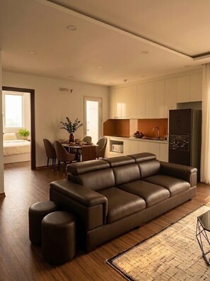 A modern living room with a leather sofa, ottomans, a dining area with chairs, a kitchen with cabinets, and a refrigerator. - VEC Homes - Near Vietnam Exposition Center VEC Dong Anh (Hanoi)