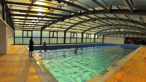 Una piscina interior con cubierta de madera, barandales metálicos y vistas a través del techo.