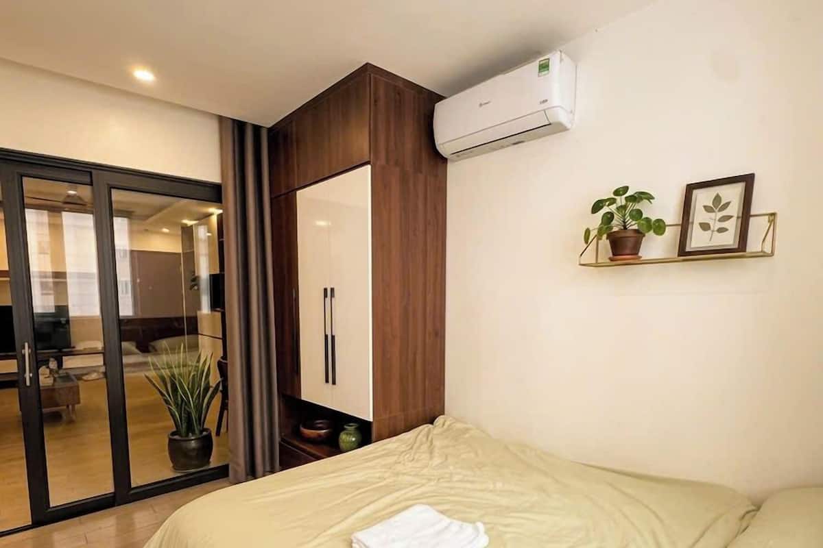 A bedroom with a bed, a potted plant, a framed picture, and an air conditioning unit.