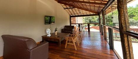 A spacious room with a wooden floor, a sofa, a table, chairs, and a TV mounted on the wall.