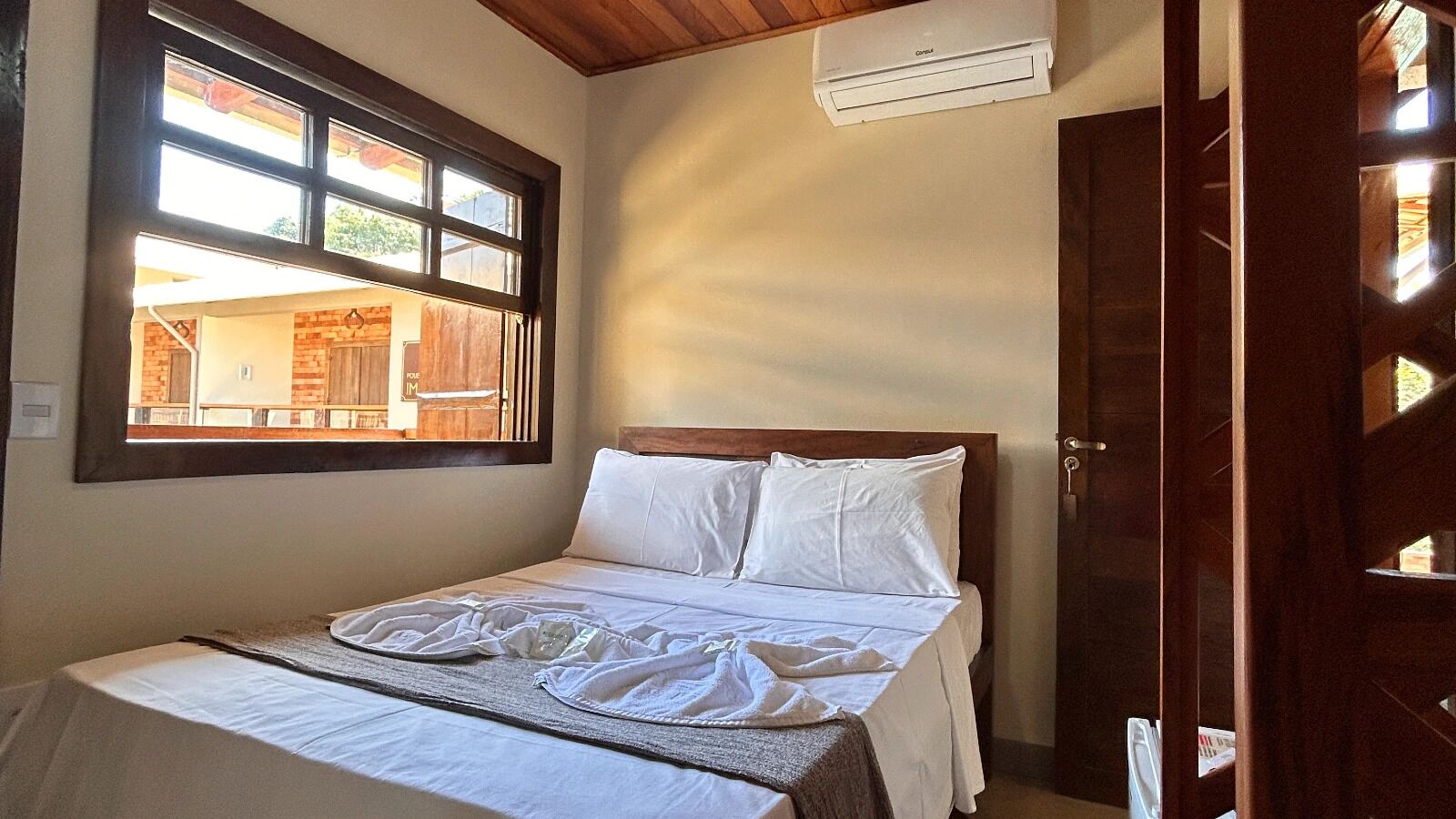 Quarto com cama, janela, ar condicionado e porta de madeira.