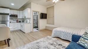 Un ambiente compatto con angolo cottura, ventilatore a soffitto, un letto con biancheria a motivi decorativi e una piccola area salotto.