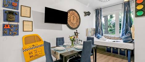 A modern room with a dining table, chairs, a bed with a view, a wall clock, and various wall decorations.