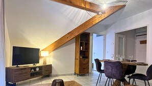 Ein modernes Wohnzimmer mit Fernseher, Holzmöbeln, einem Essbereich mit Stühlen und einer Treppe.