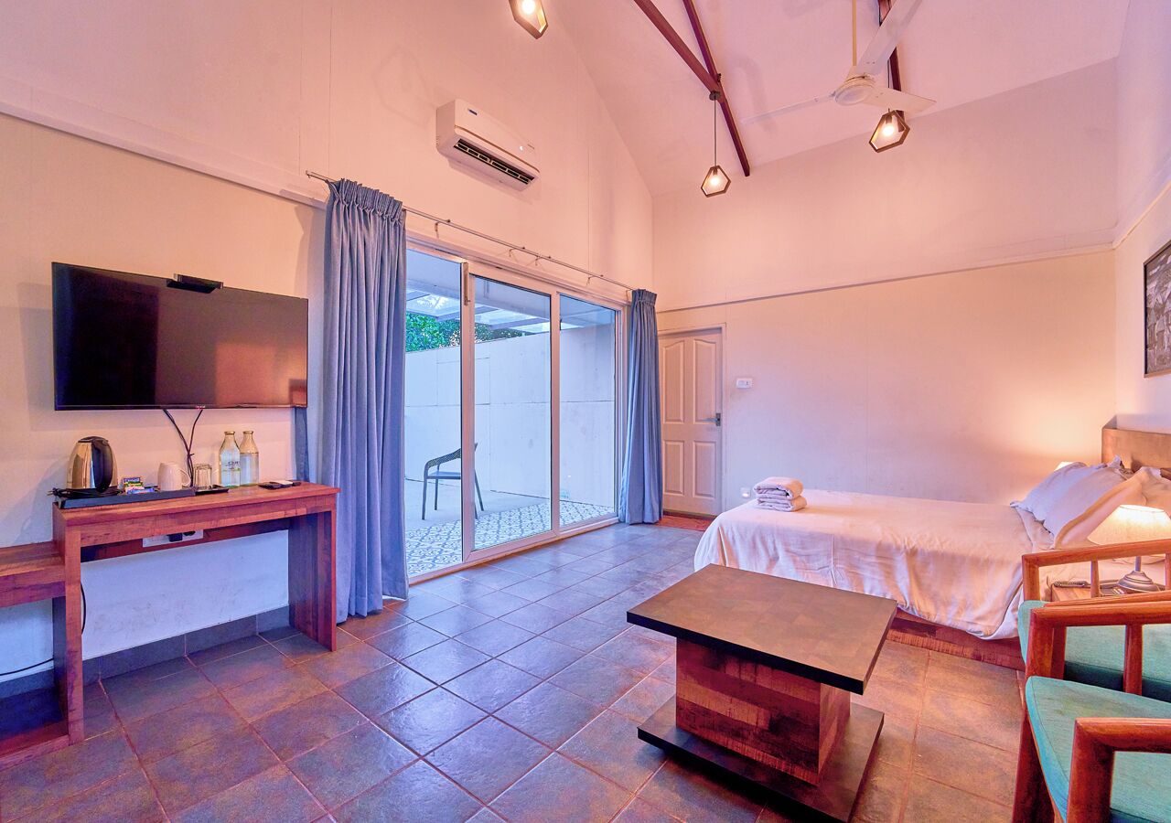 Una habitación con cama, escritorio, televisor y puerta corrediza de vidrio que da a un área exterior.