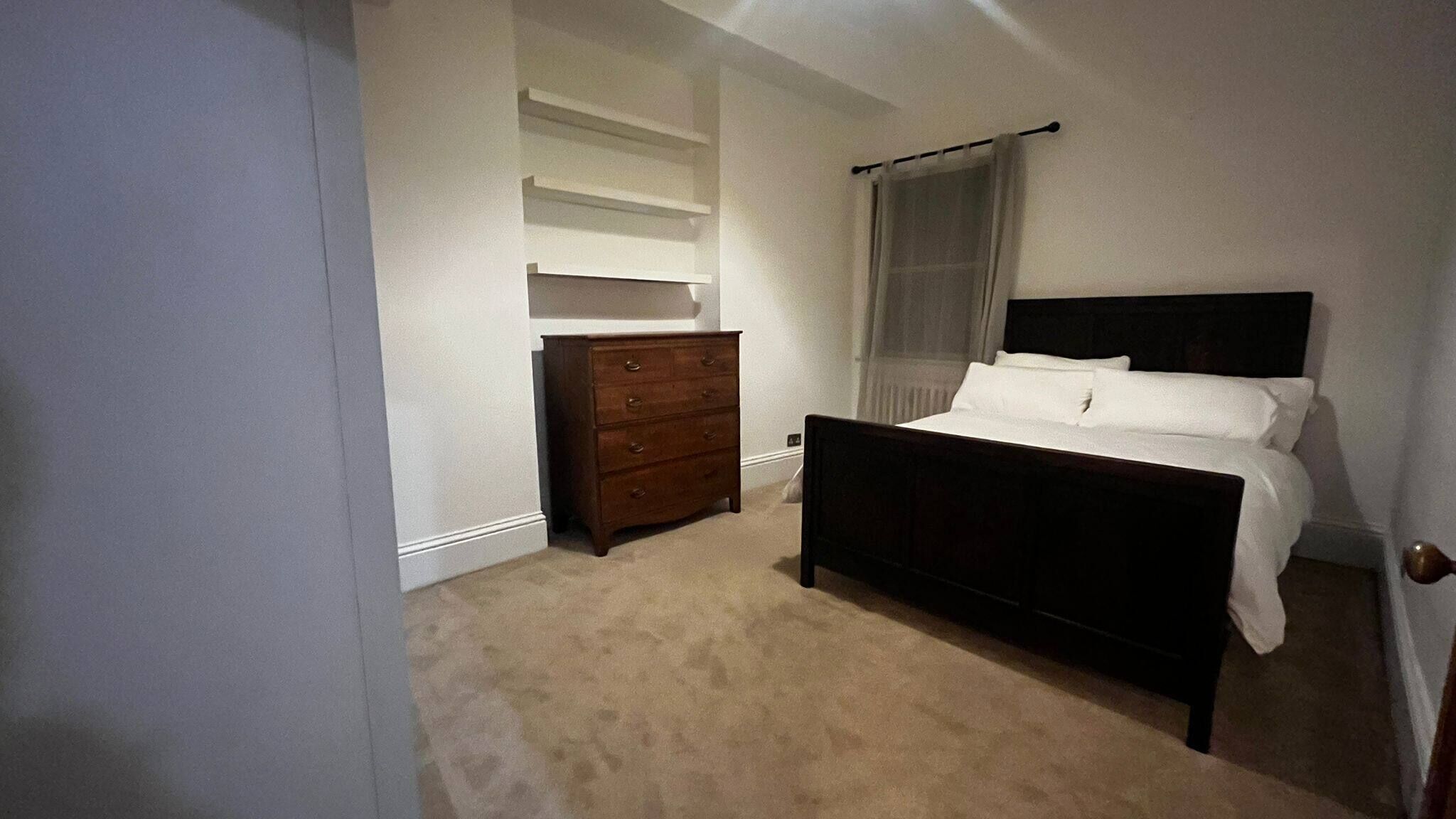 A bedroom with a bed, a dresser, a window with curtains, and a carpeted floor.