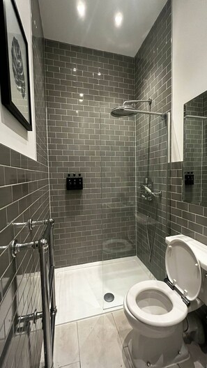 A modern bathroom with a shower, toilet, and a tiled floor. - Charming Victorian Flat With Private Garden in Shepherd's Bush (London)